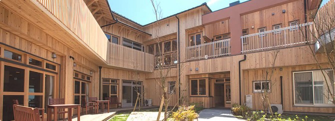木造建築に囲まれた中庭。緑地と季節の樹木が配置された落ち着いた空間。